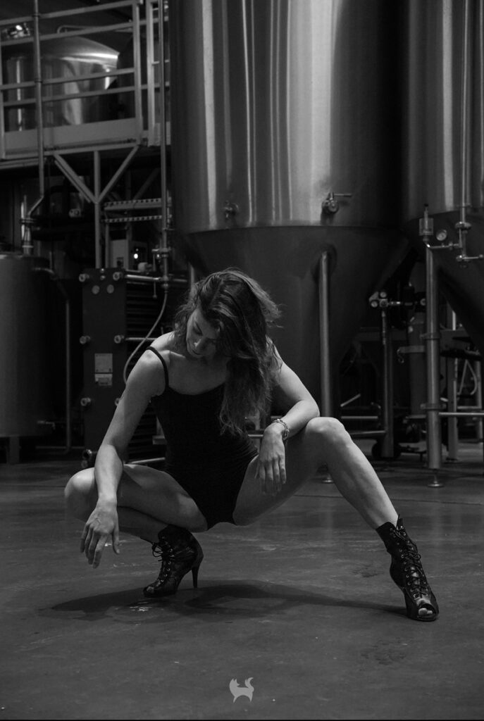 Danseuse de heels en noir et blanc, posant en talons hauts dans un décor industriel.