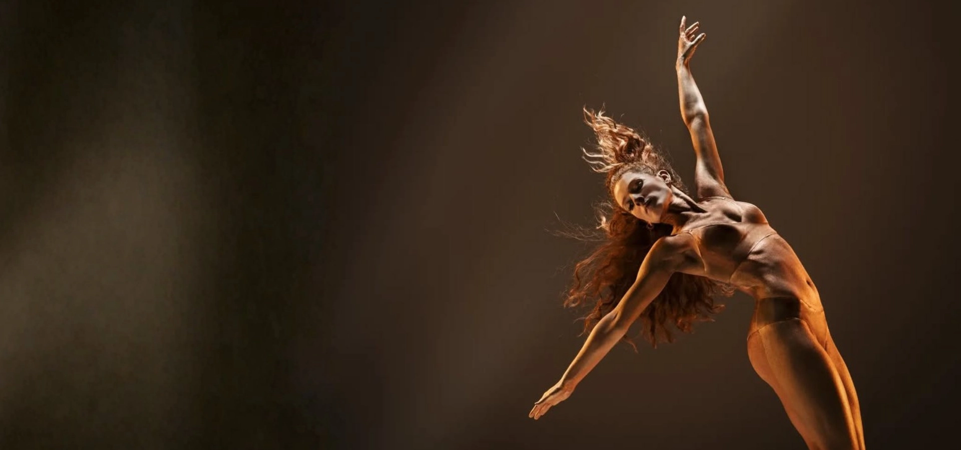 Danseuse en mouvement sur scène, éclairée par une lumière chaude, exprimant grâce et puissance corporelle à travers la danse contemporaine.