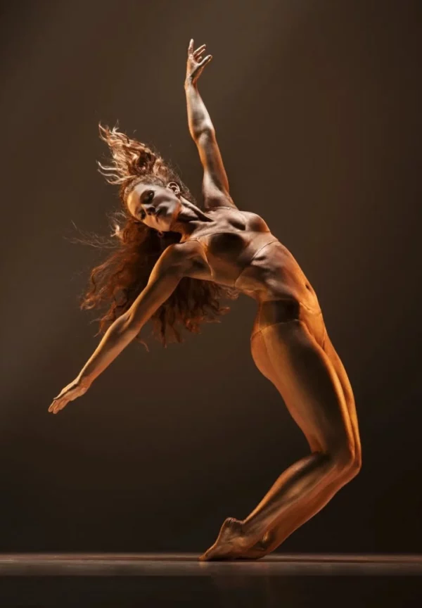 Danseuse en mouvement, cambrée et en extension, éclairée par une lumière dorée, exprimant liberté et puissance à travers la danse contemporaine.