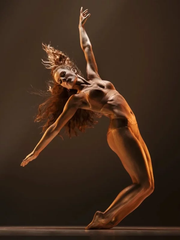 Danseuse en mouvement, cambrée et en extension, éclairée par une lumière dorée, exprimant liberté et puissance à travers la danse contemporaine.